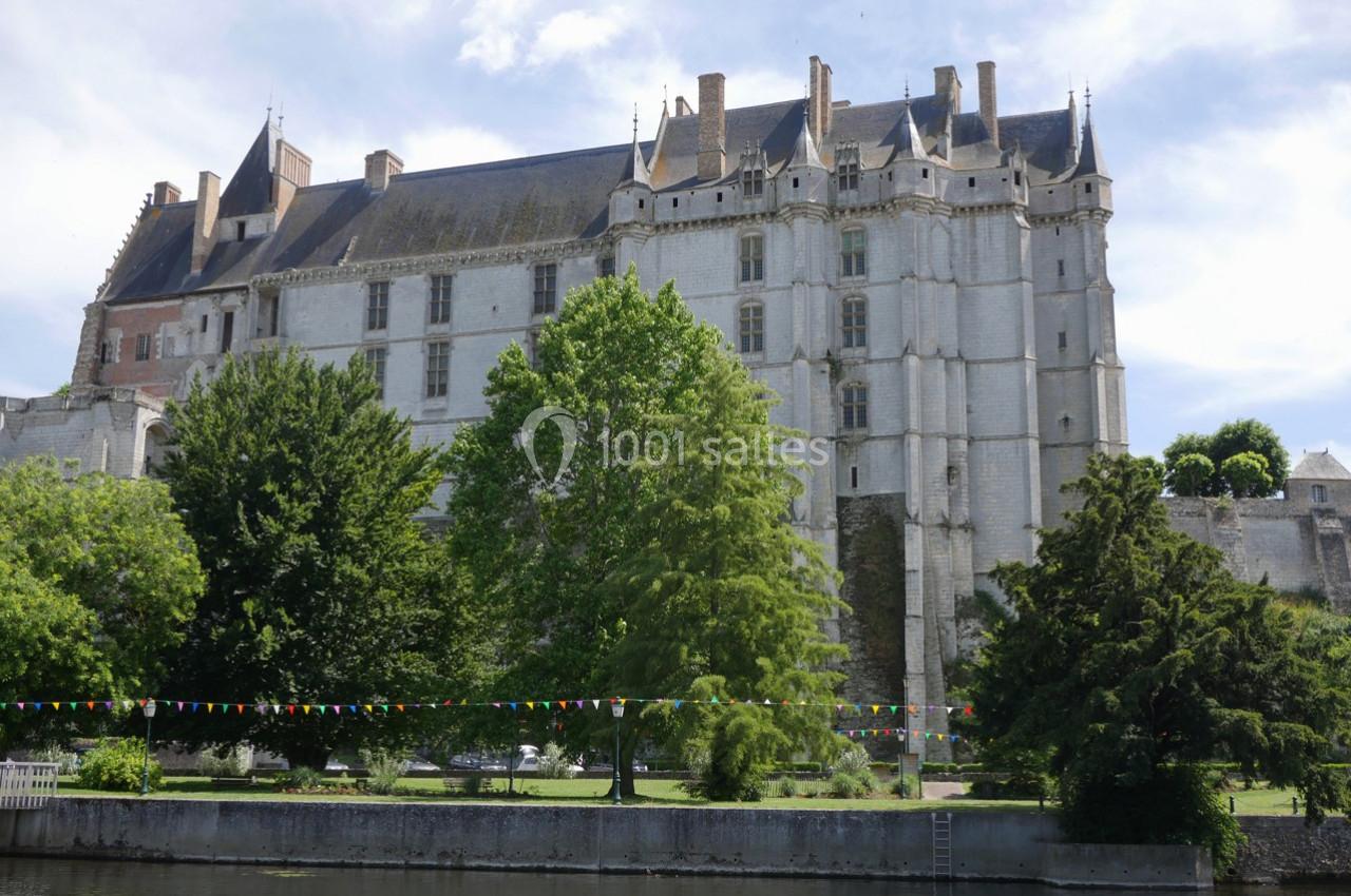 Château en pierre blanche entouré d'arbres, situé au bord d'une rivière, avec des guirlandes colorées suspendues.