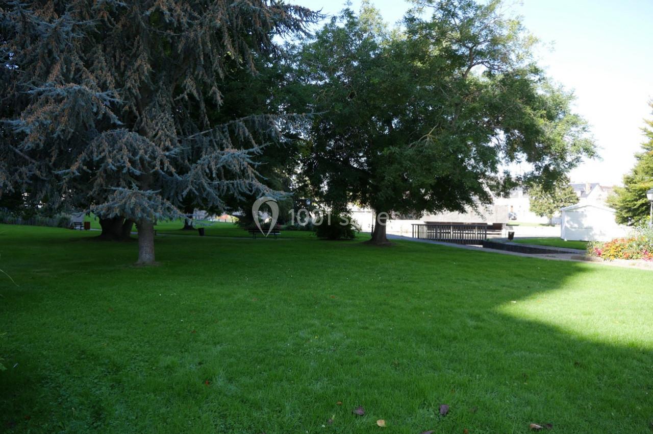Pelouse verte entourée d'arbres avec un chemin pavé et des bâtiments en arrière-plan sous un ciel dégagé.