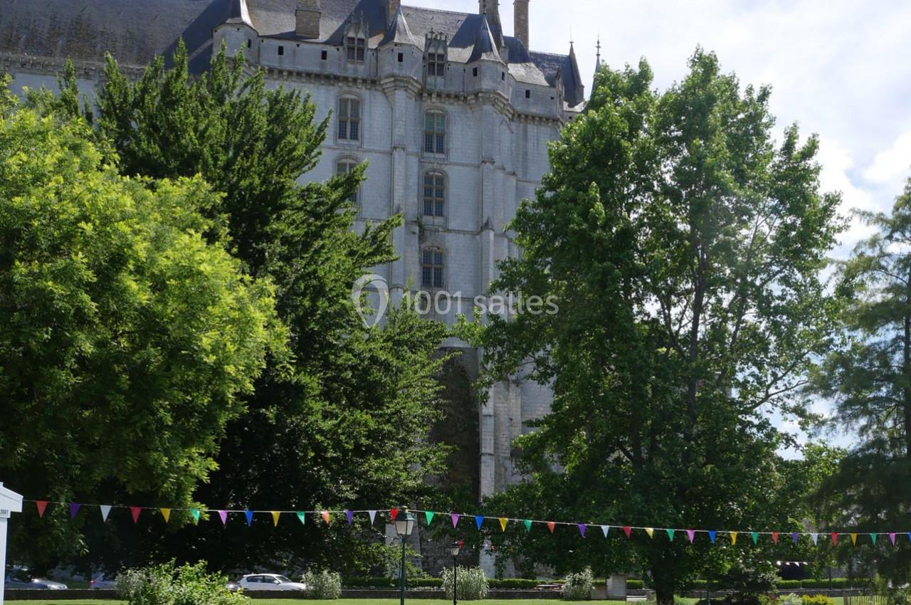 Façade d'un château en pierre entouré d'arbres et de verdure, avec des fanions colorés suspendus au premier plan.
