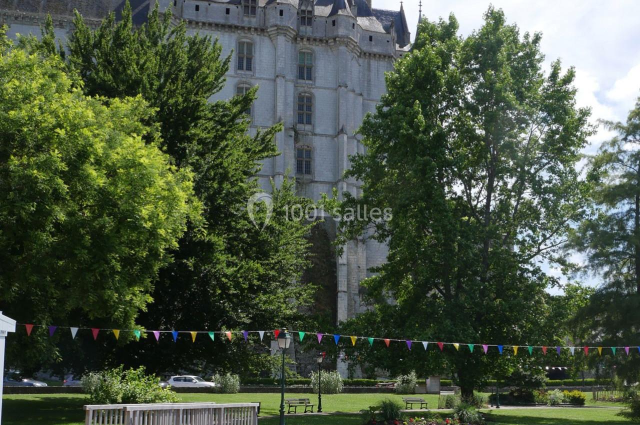 Façade d'un château en pierre entouré d'arbres, avec un parc aménagé et des guirlandes colorées au premier plan.
