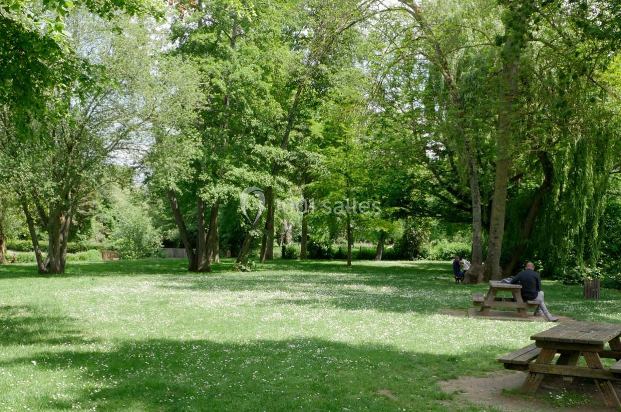 Espace vert avec pelouse, arbres et tables de pique-nique, quelques personnes assises dans un cadre paisible.