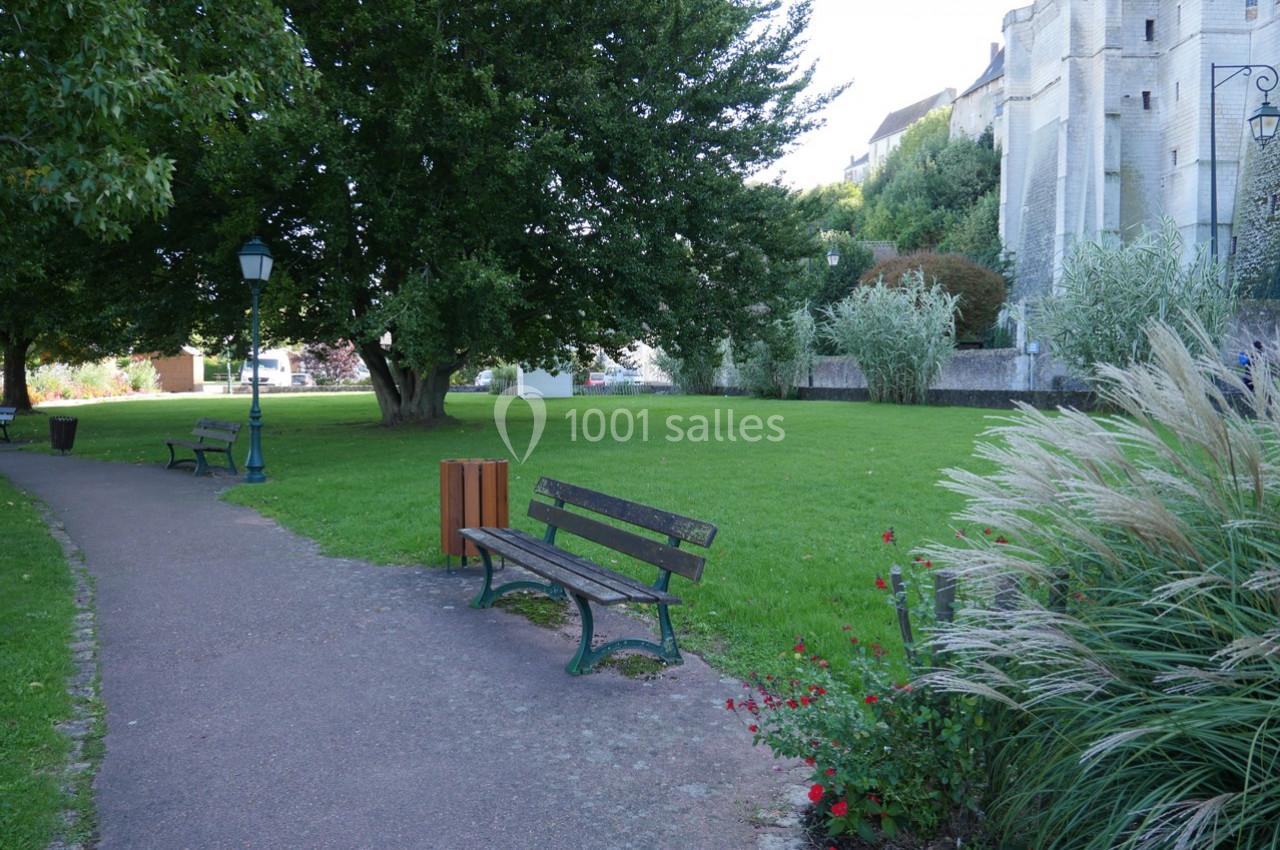Allée bordée de bancs et de verdure dans un parc, avec un bâtiment en pierre visible en arrière-plan.