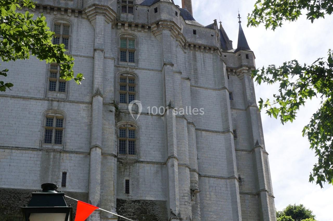 Façade d'un château en pierre blanche avec des tours et des fenêtres, entouré de feuillage et de fanions colorés.