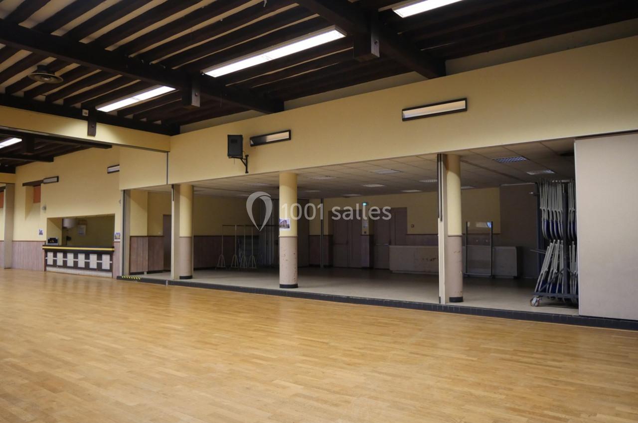 Salle spacieuse avec parquet en bois clair, murs beiges, miroirs et plafond à poutres apparentes.
