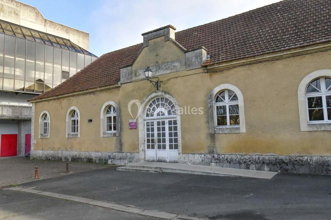 Bâtiment ancien avec façade en pierre et toit en tuiles, fenêtres cintrées et porte centrale vitrée.