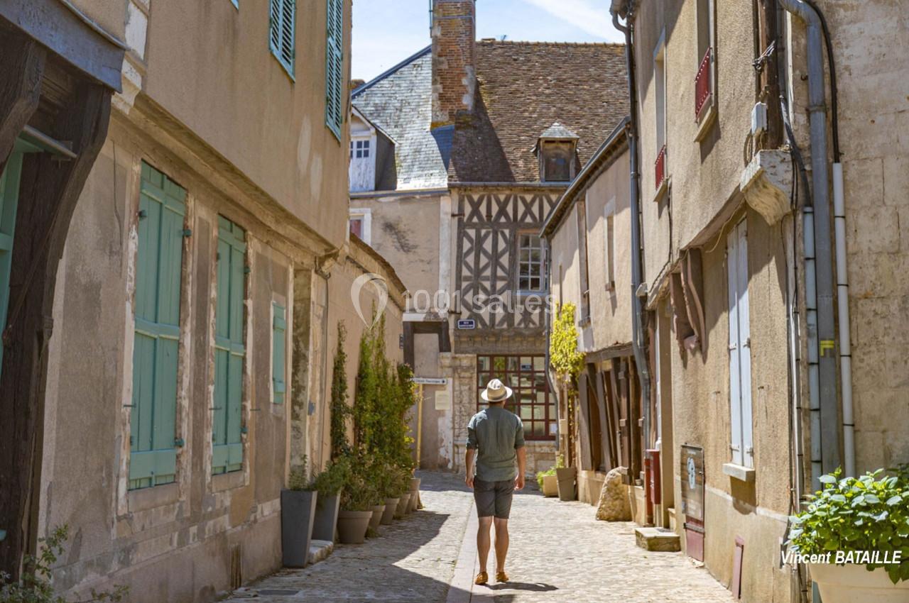 Un homme marche dans une ruelle pavée bordée de maisons anciennes aux façades en pierre et à colombages.