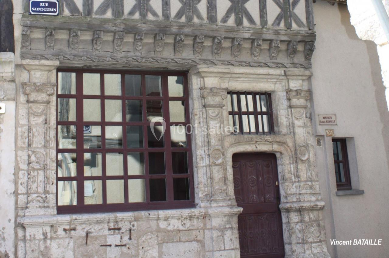 Façade en pierre d'une maison ancienne avec colombages, fenêtres à carreaux et porte sculptée.