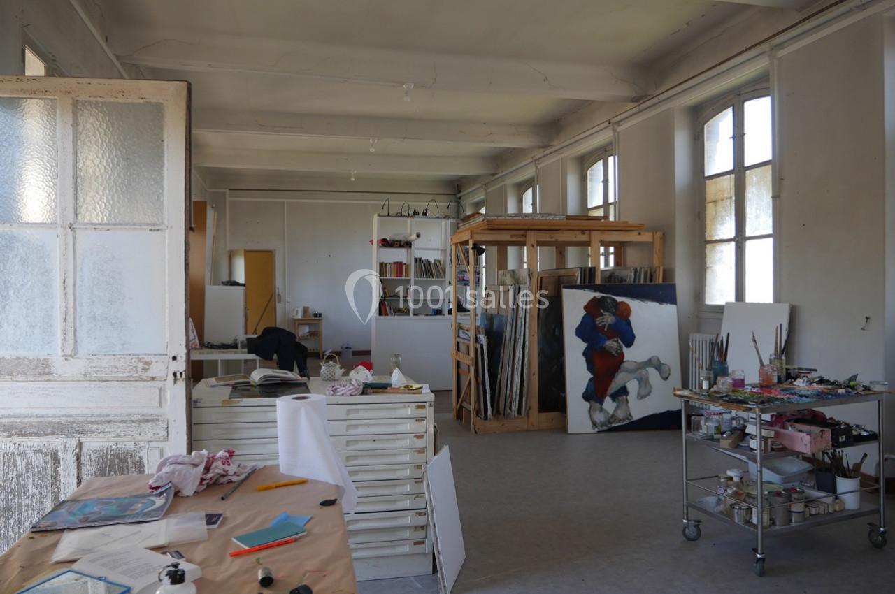 Atelier d'artiste lumineux avec tables de travail, matériel de peinture, étagères et une toile en cours.