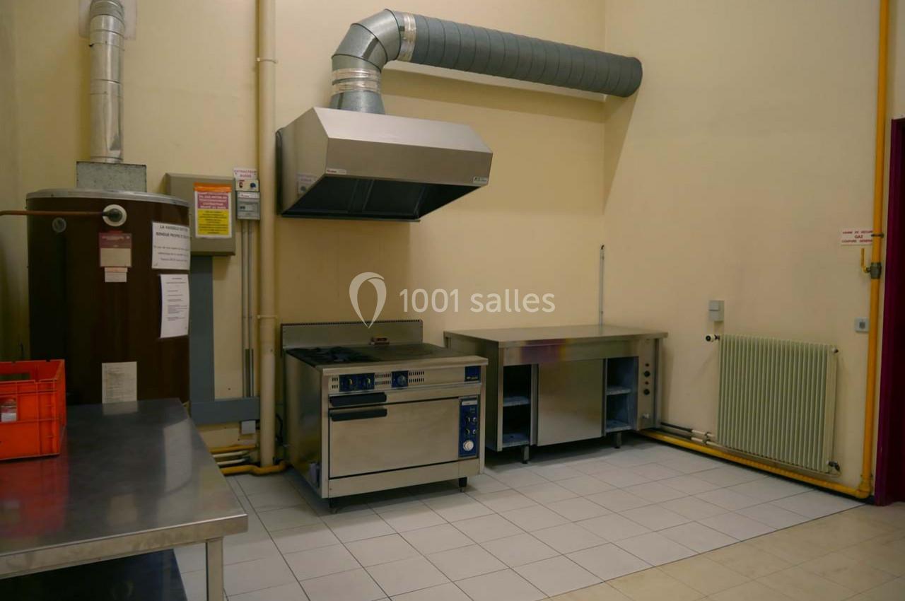 Cuisine professionnelle avec hotte, plaques de cuisson, plans de travail en inox et carrelage au sol.