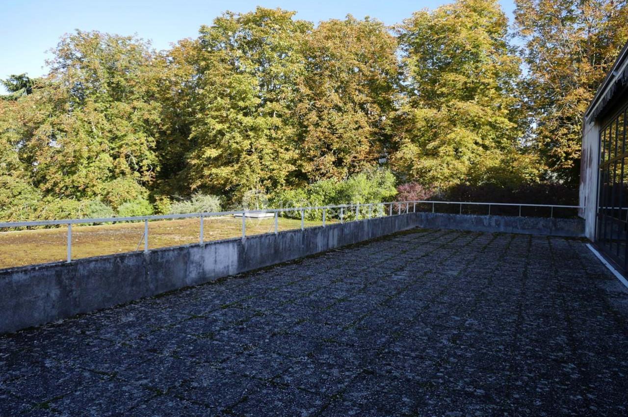 Terrasse en béton avec garde-corps métalliques, entourée d'arbres aux feuillages d'automne sous un ciel dégagé.