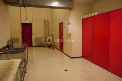 Salle de service avec éviers en inox, armoires rouges, échelle et murs beige clair.