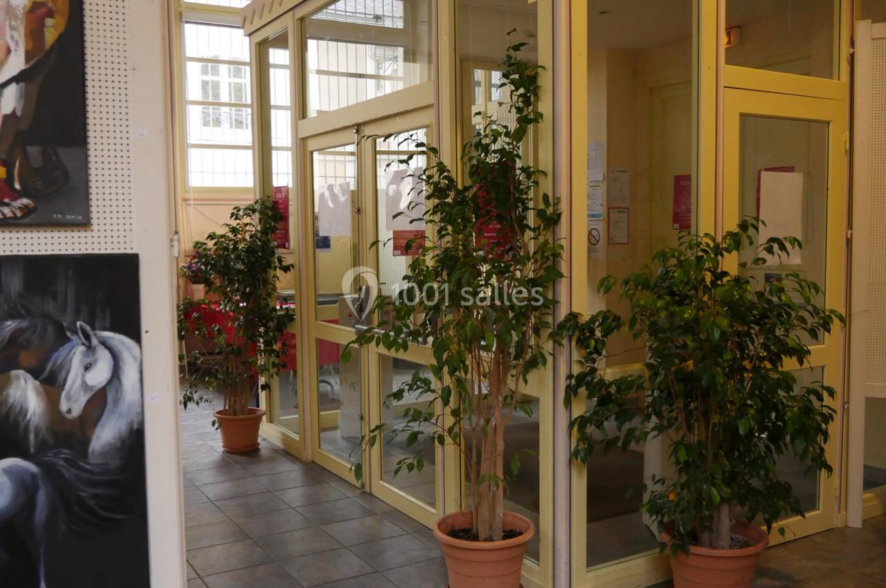 Entrée vitrée d'un bâtiment avec des plantes en pot et des peintures accrochées aux murs.