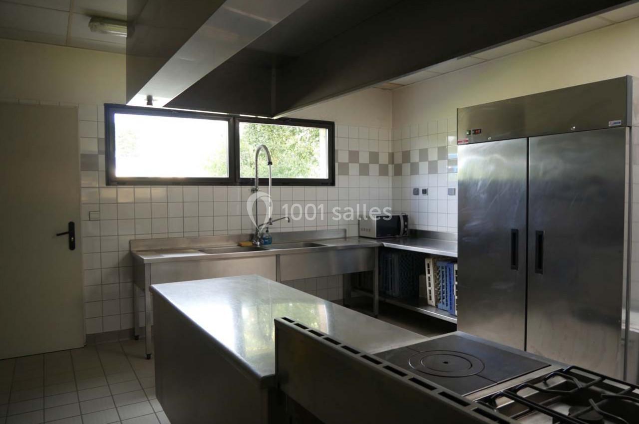 Cuisine professionnelle avec plan de travail en inox, évier, réfrigérateur, four et plaques de cuisson.