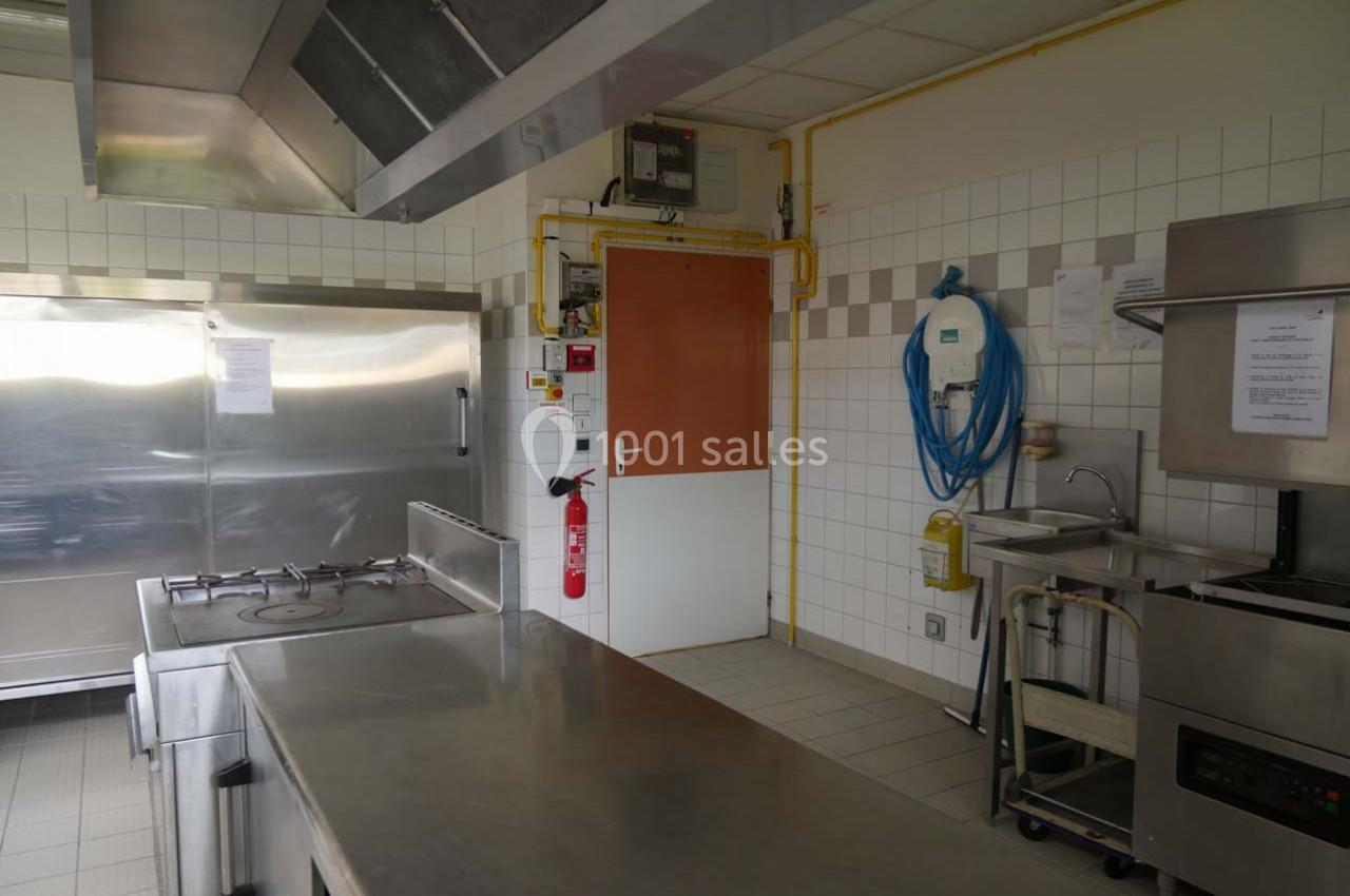 Cuisine professionnelle avec plan de travail en inox, plaques de cuisson, évier, et équipements muraux.