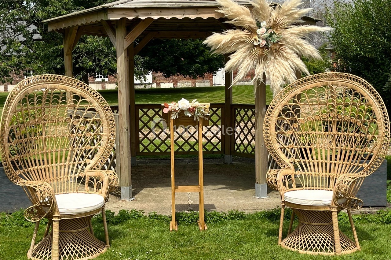 Deux fauteuils en rotin et un pupitre décoré de fleurs devant une pergola en bois dans un jardin.