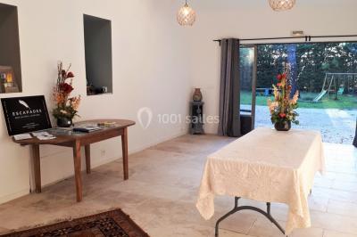 Des personnes assises sur des tapis et des chaises dans une salle lumineuse avec un tableau et des rideaux.