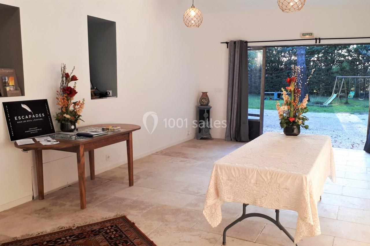 Salle lumineuse avec table décorée de fleurs, vue sur un jardin avec balançoire à travers une baie vitrée ouverte.