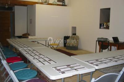 Des personnes assises sur des tapis et des chaises dans une salle lumineuse avec un tableau et des rideaux.