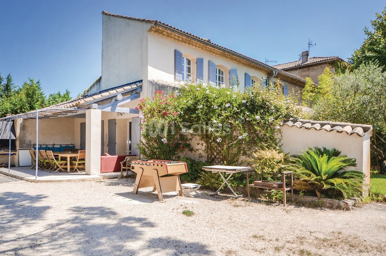 Maison provençale avec terrasse ombragée, mobilier de jardin, table de ping-pong et végétation environnante.