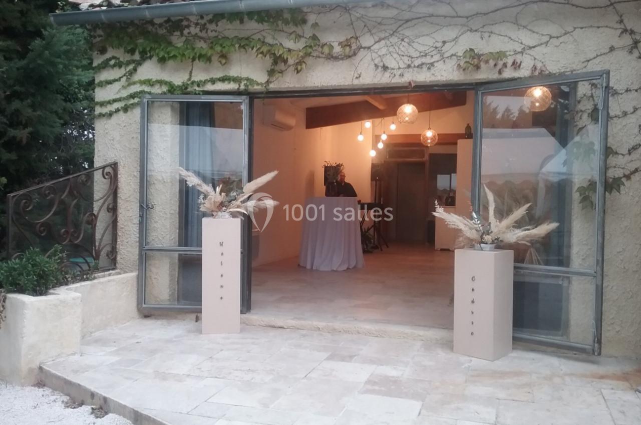 Entrée d'une salle avec portes vitrées ouvertes, décorée de plantes séchées et éclairée par des suspensions lumineuses.