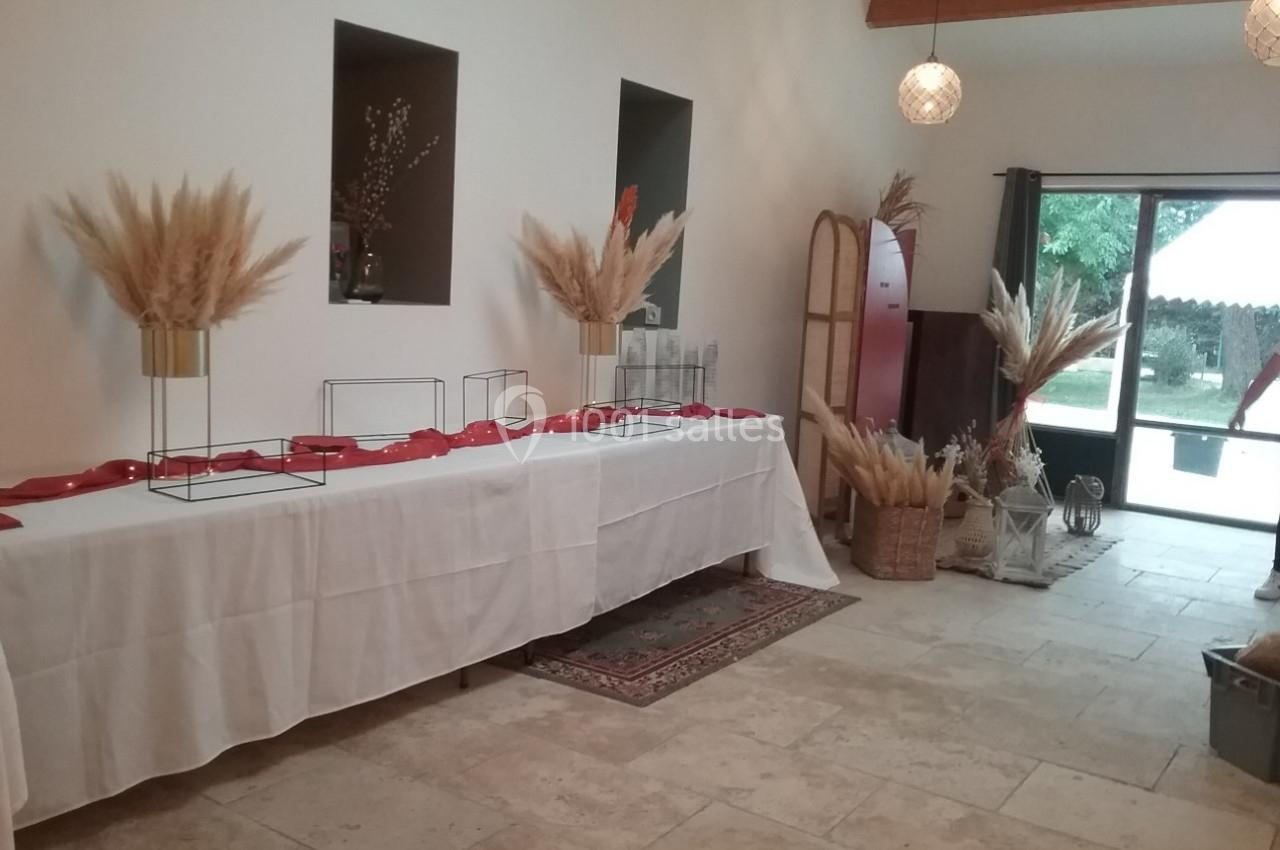 Salle lumineuse décorée avec des pampas, une table recouverte d'une nappe blanche et des rubans rouges.
