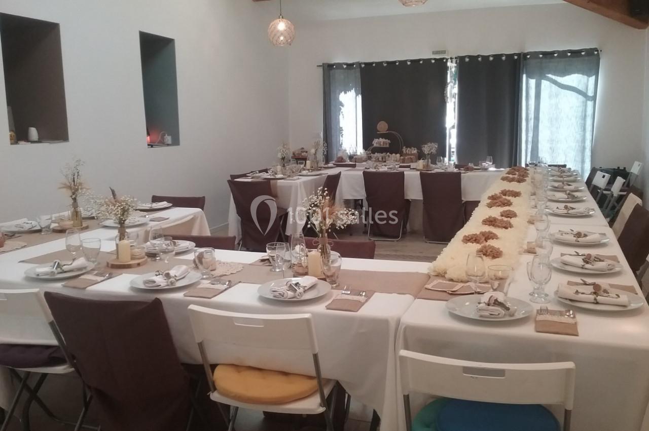 Salle décorée pour un repas, avec tables en U, nappes blanches, décorations florales et vaisselle dressée.