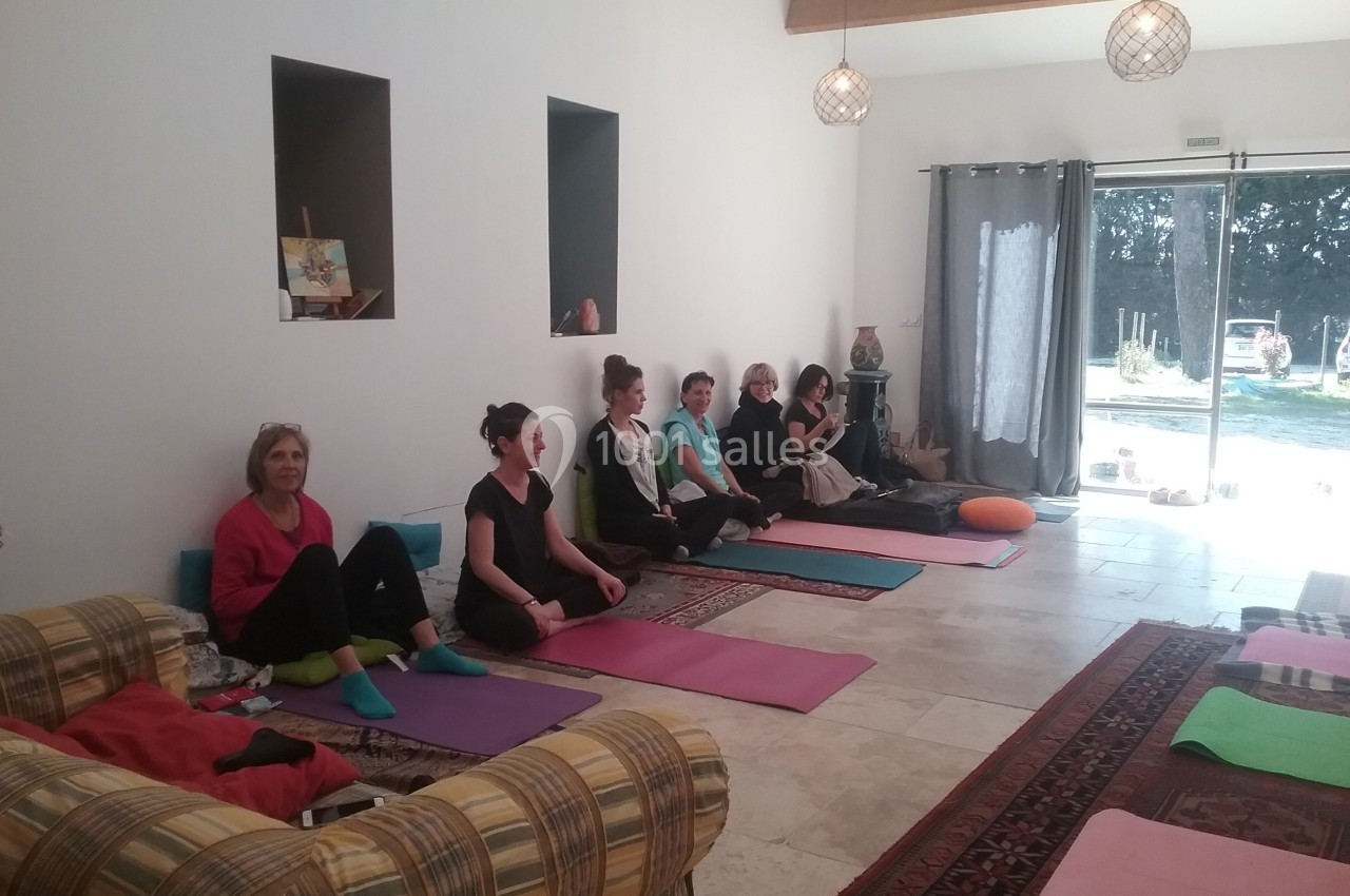 Des personnes assises sur des tapis de yoga dans une salle lumineuse avec des coussins et des décorations simples.