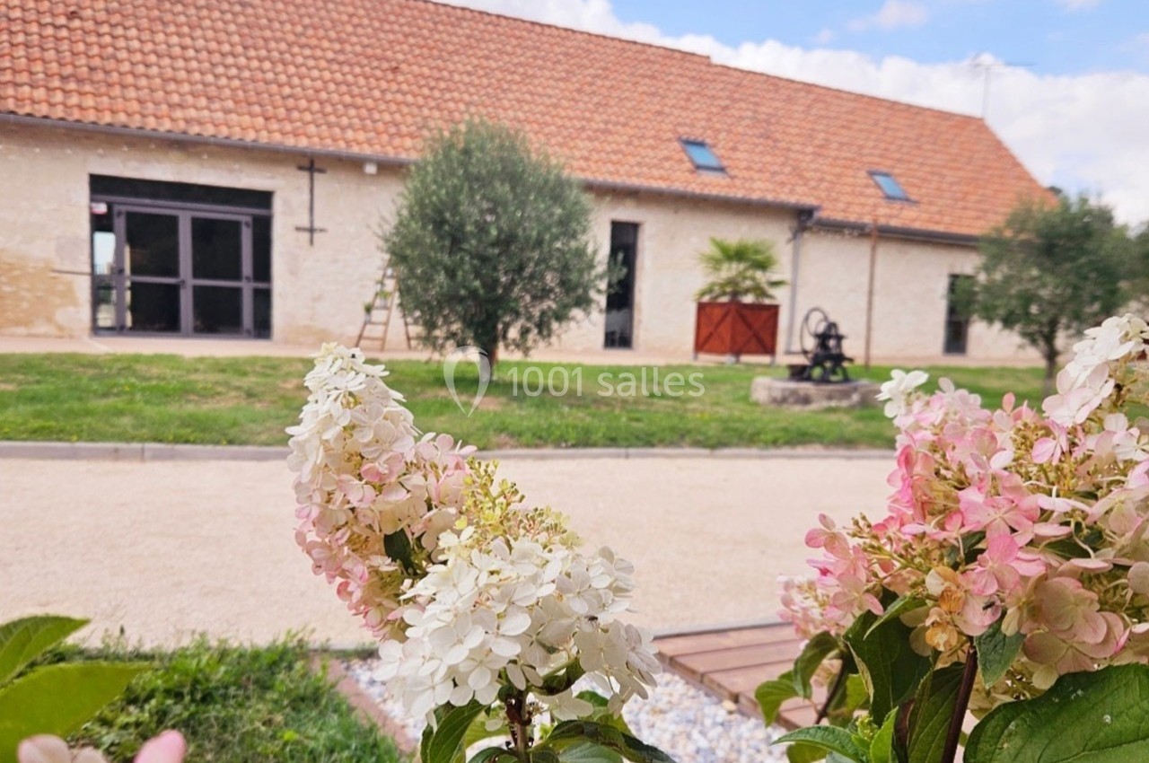 Façade d'un bâtiment en pierre avec toit en tuiles, entouré de verdure et hortensias au premier plan.