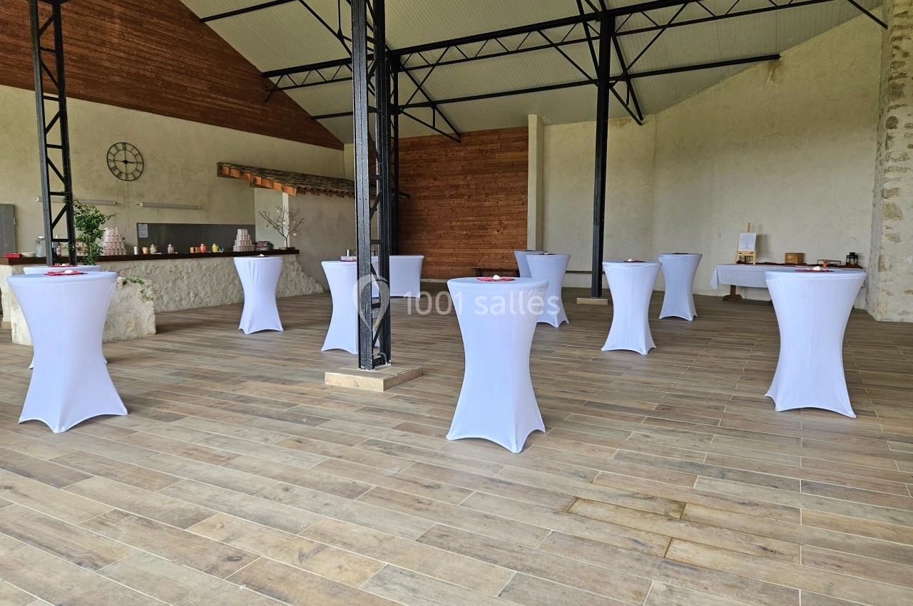 Salle avec des tables hautes drapées de blanc, disposées sur un sol en bois dans un espace lumineux et ouvert.