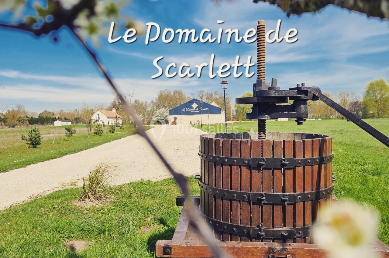 Presse à vin en bois dans un paysage champêtre avec un chemin menant à des bâtiments au loin.