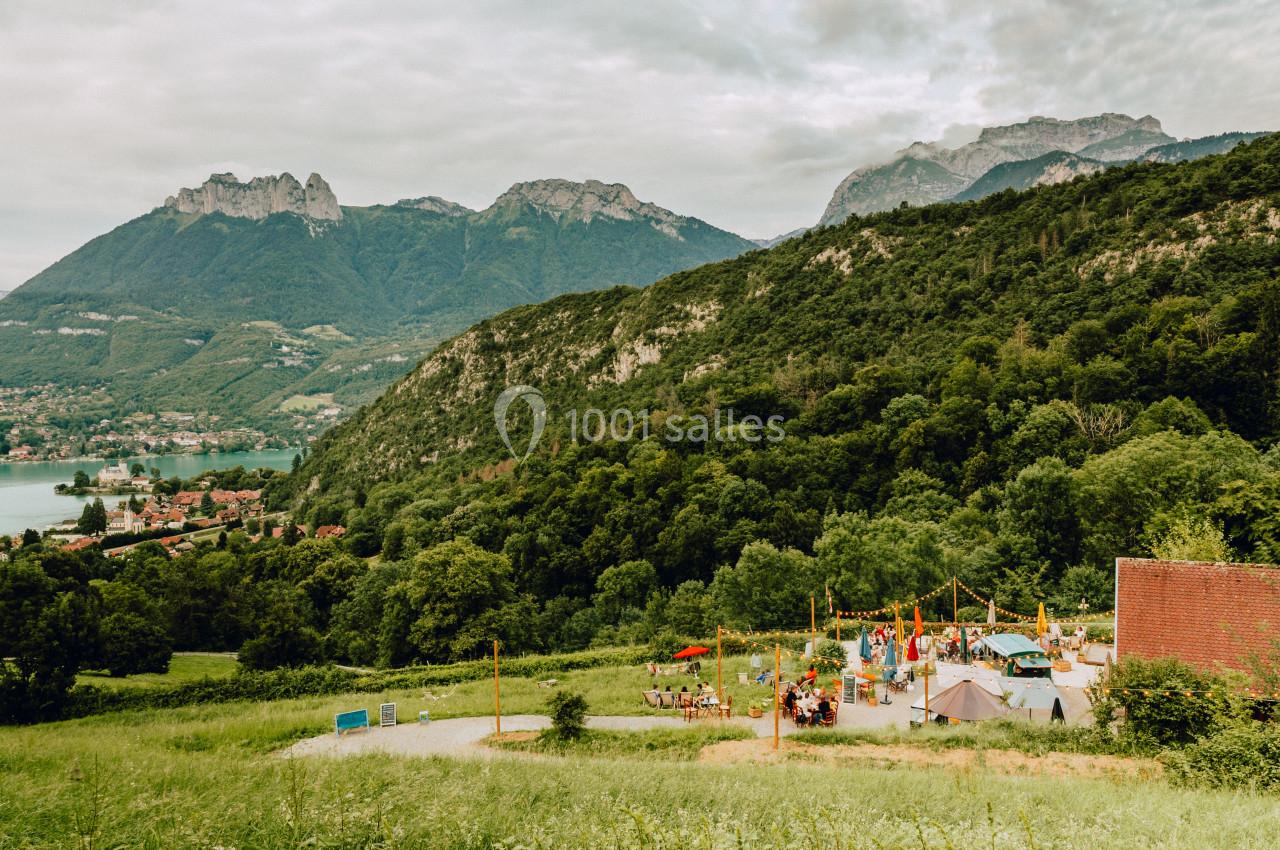 Vue d'un terrain de jeux animé entouré de collines verdoyantes, avec un lac et des montagnes en arrière-plan.