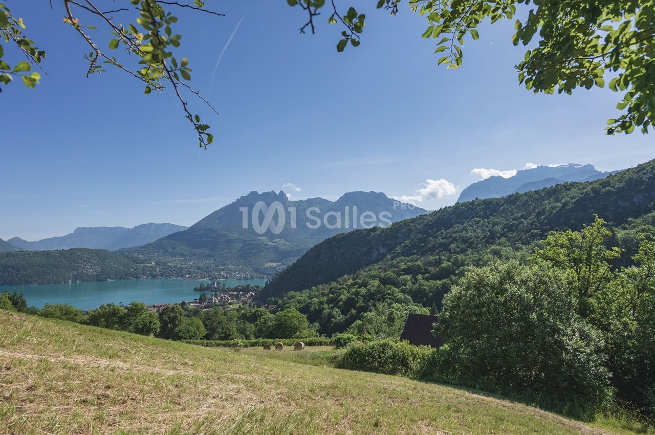 Paysage de montagne avec un lac turquoise, des collines verdoyantes et un ciel bleu dégagé.