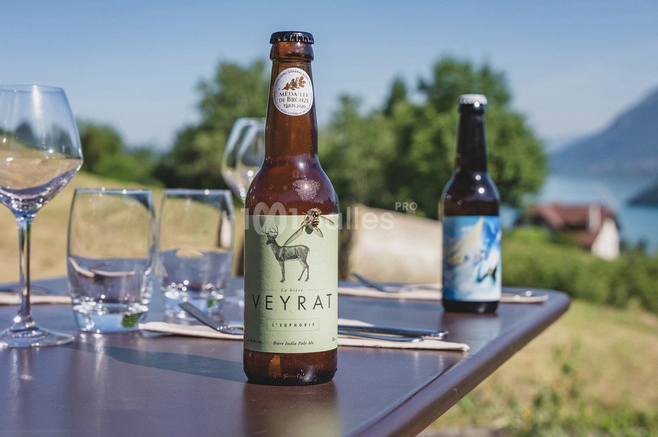 Bouteille de bière artisanale posée sur une table en extérieur avec vue sur un paysage naturel et des verres.