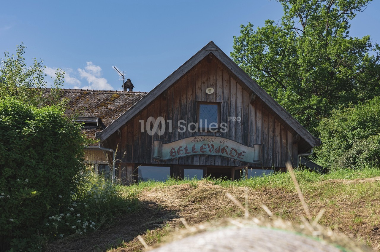 Façade en bois d'une maison rurale entourée de végétation sous un ciel bleu.