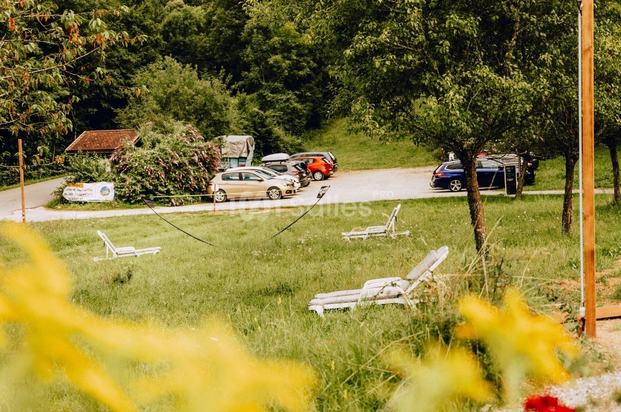 Des chaises longues blanches disposées sur une pelouse verdoyante près d'un parking entouré d'arbres.
