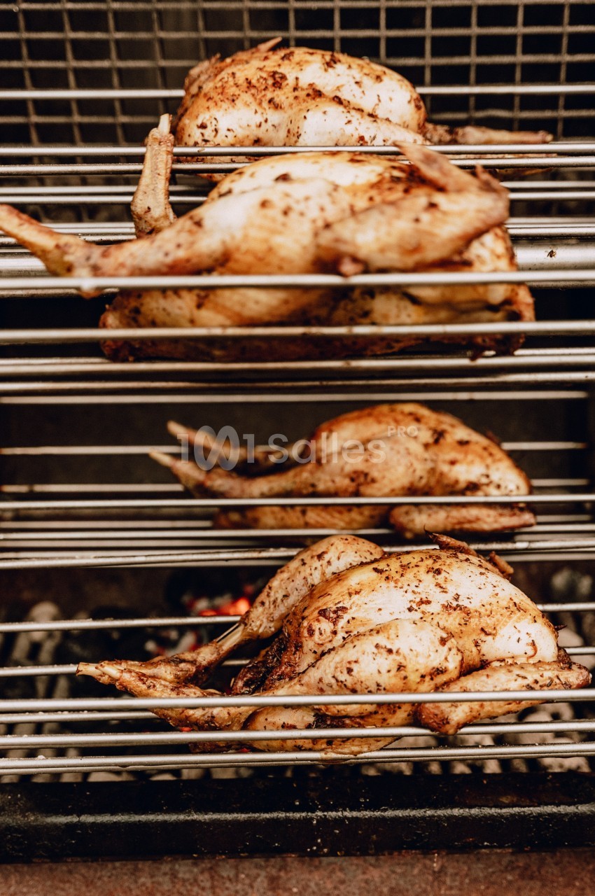 Poulets entiers assaisonnés rôtissant sur des broches au-dessus de braises dans un grill.