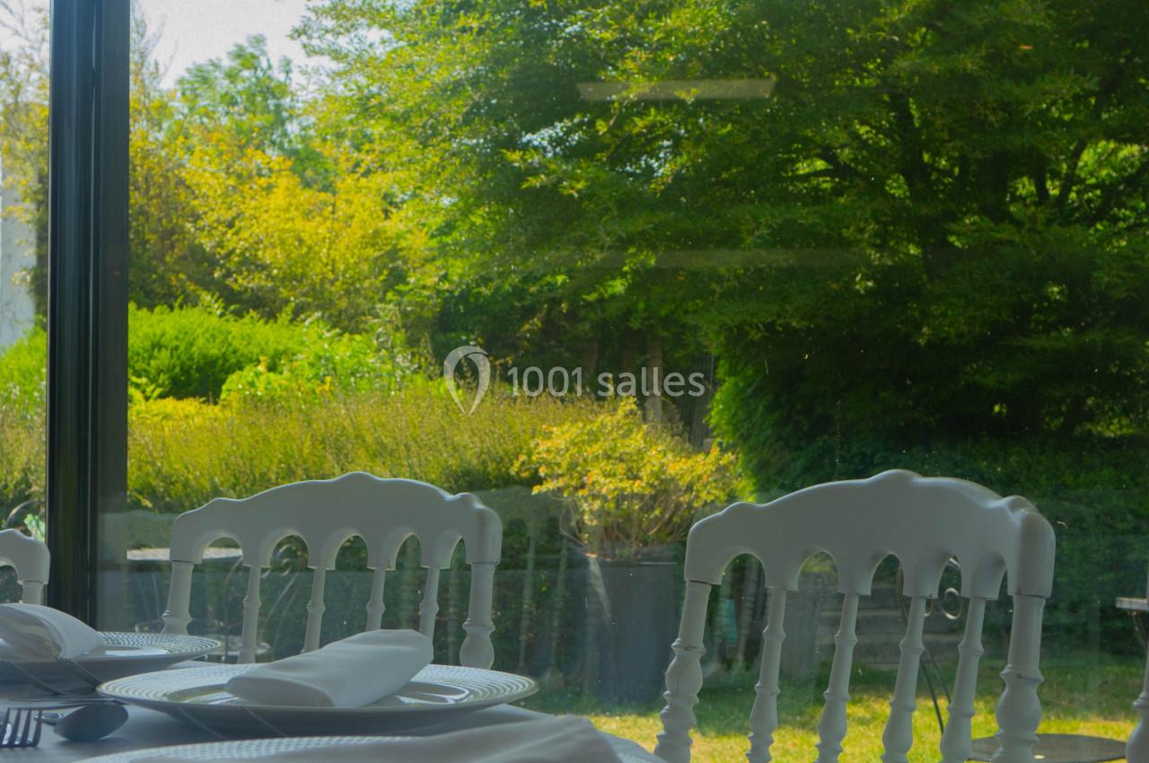 Salle de restaurant avec table dressée, vue sur un jardin verdoyant à travers une grande baie vitrée.