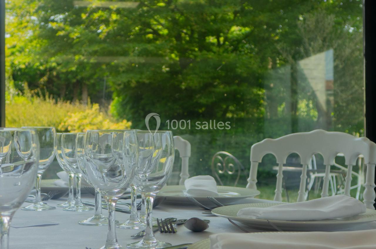 Table dressée avec vaisselle et verres élégants, vue sur un jardin verdoyant à travers une grande baie vitrée.