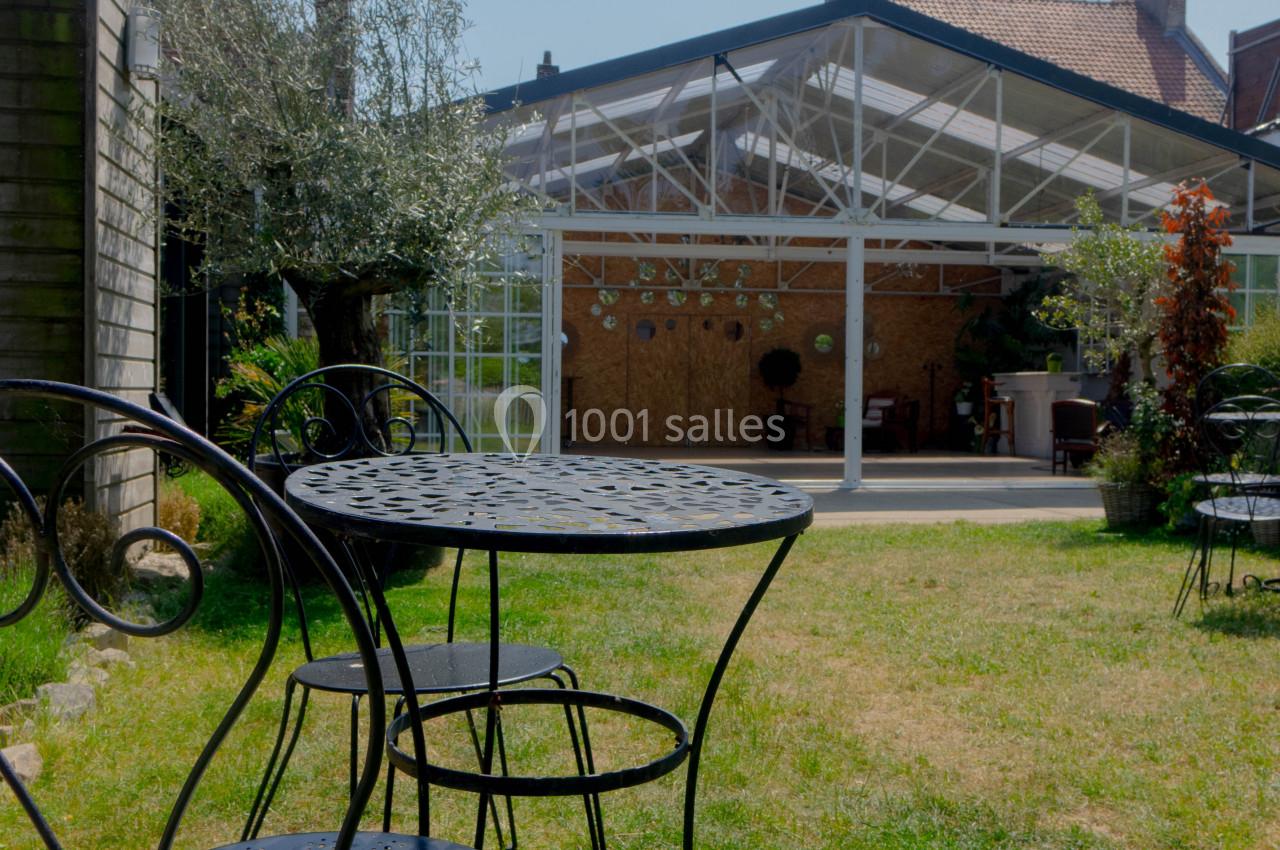 Table et chaises en métal noir sur une pelouse, avec une verrière et des bâtiments en arrière-plan.