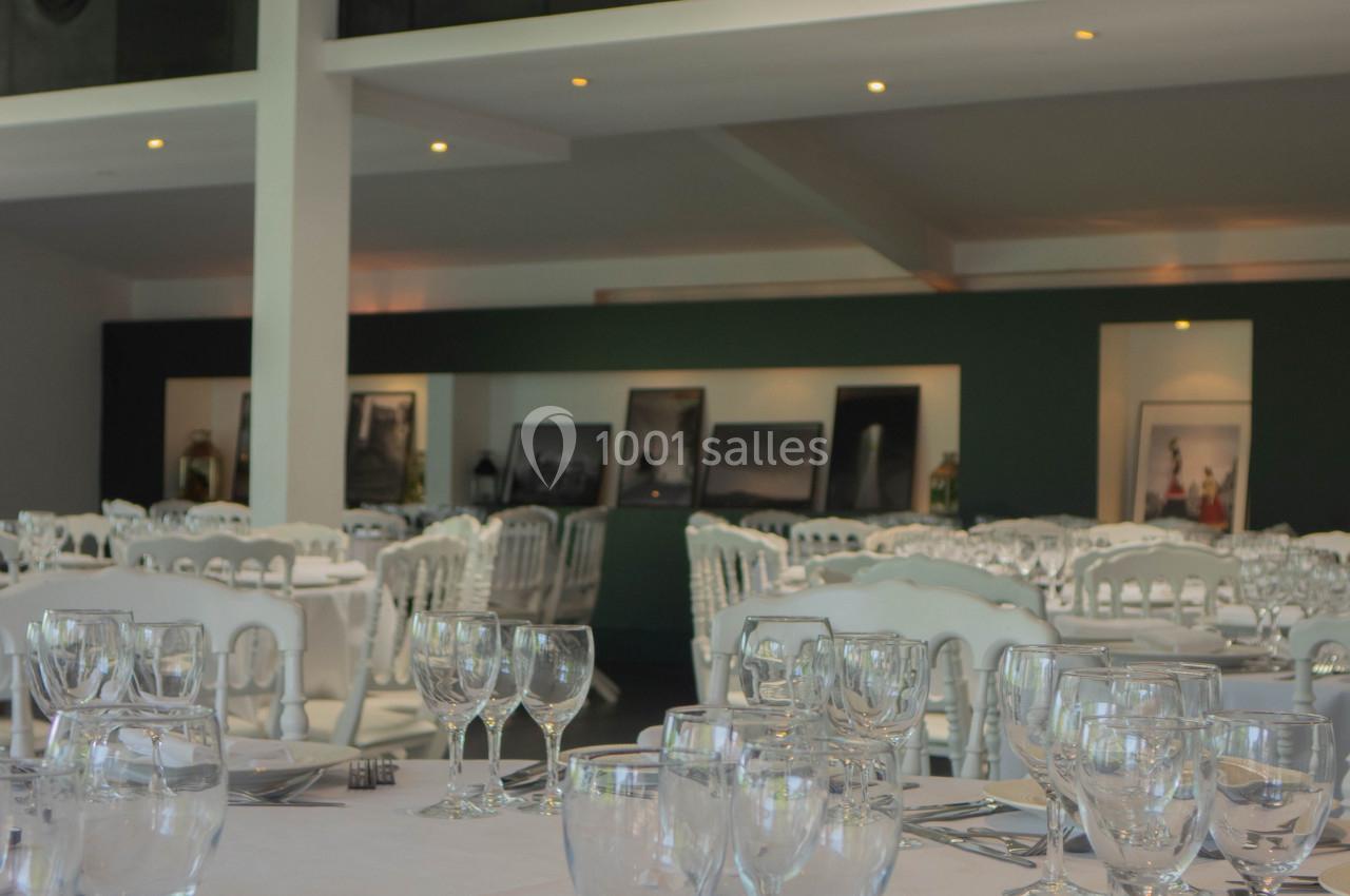 Salle de réception lumineuse avec tables dressées, nappes blanches, verres et couverts, décor sobre en arrière-plan.