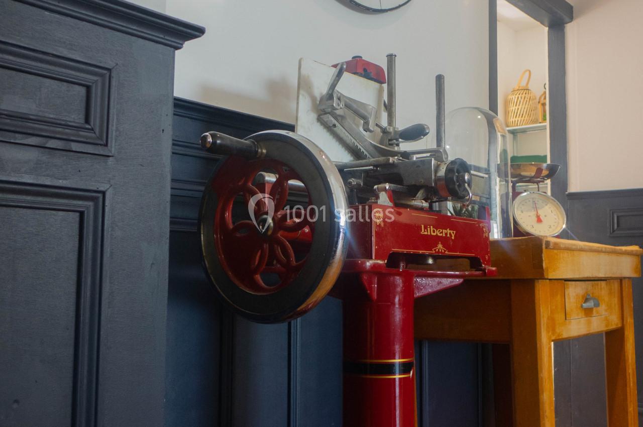Machine à trancher rouge vintage posée près d'une table en bois, avec une grande horloge murale en arrière-plan.