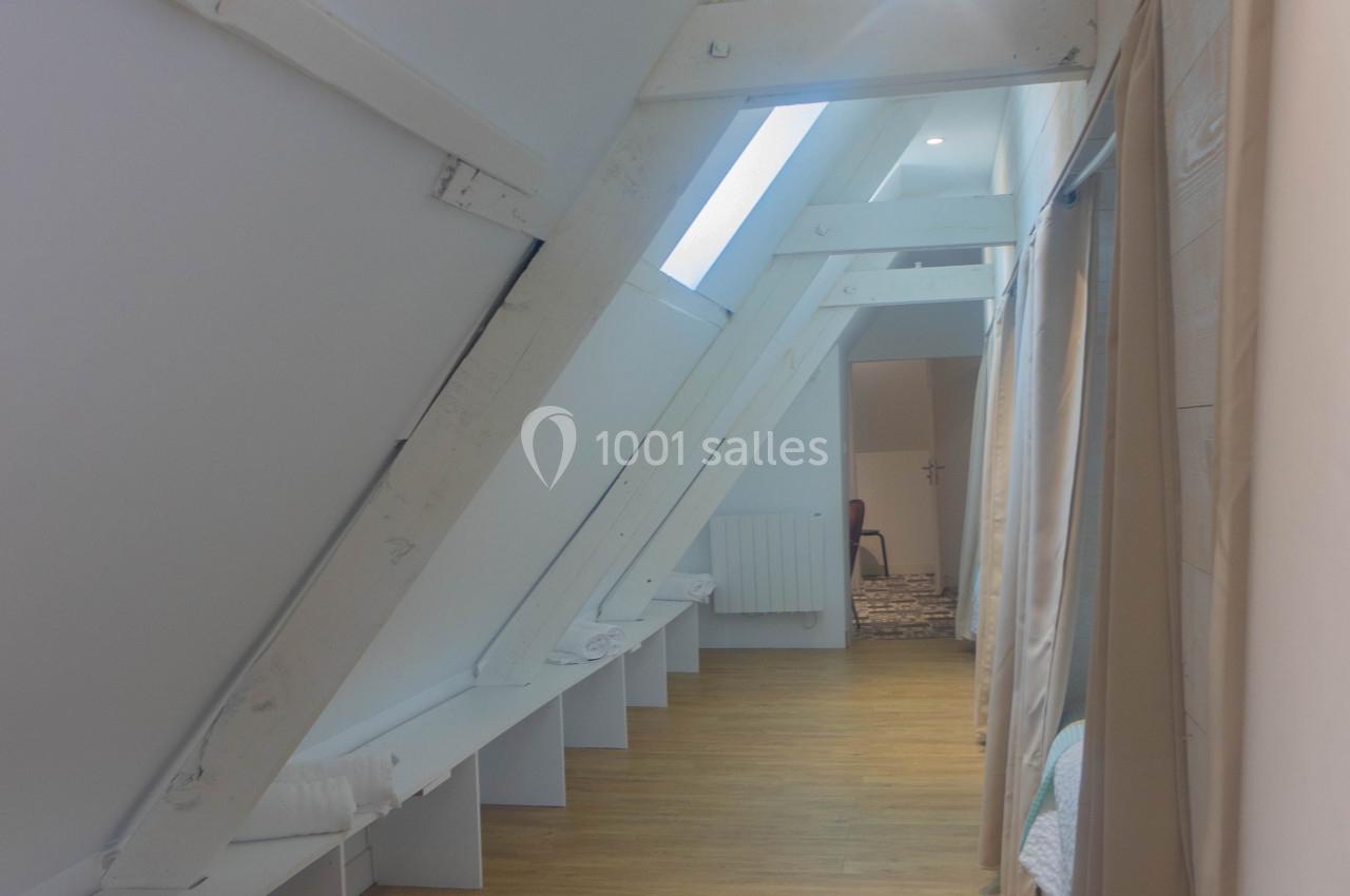 Couloir mansardé avec poutres apparentes blanches, parquet clair et rideaux séparant des espaces.