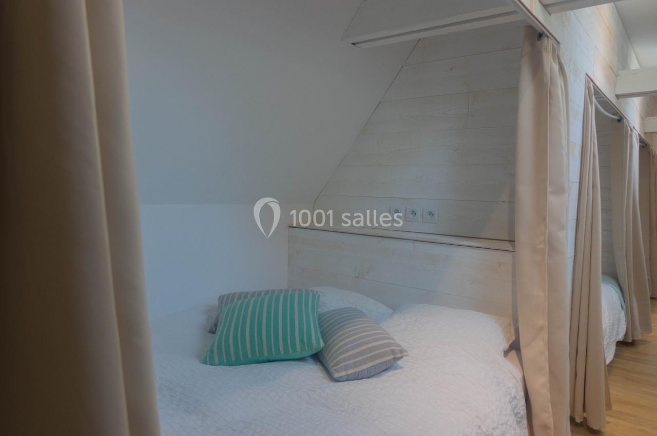 Lit avec des coussins colorés dans une alcôve en bois clair, séparée par des rideaux beiges.