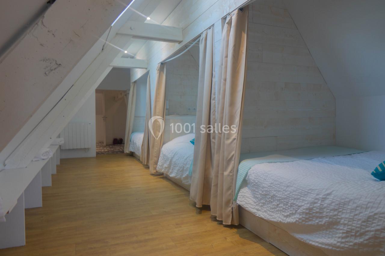 Chambre mansardée avec lits alignés séparés par des rideaux, parquet au sol et murs en bois clair.