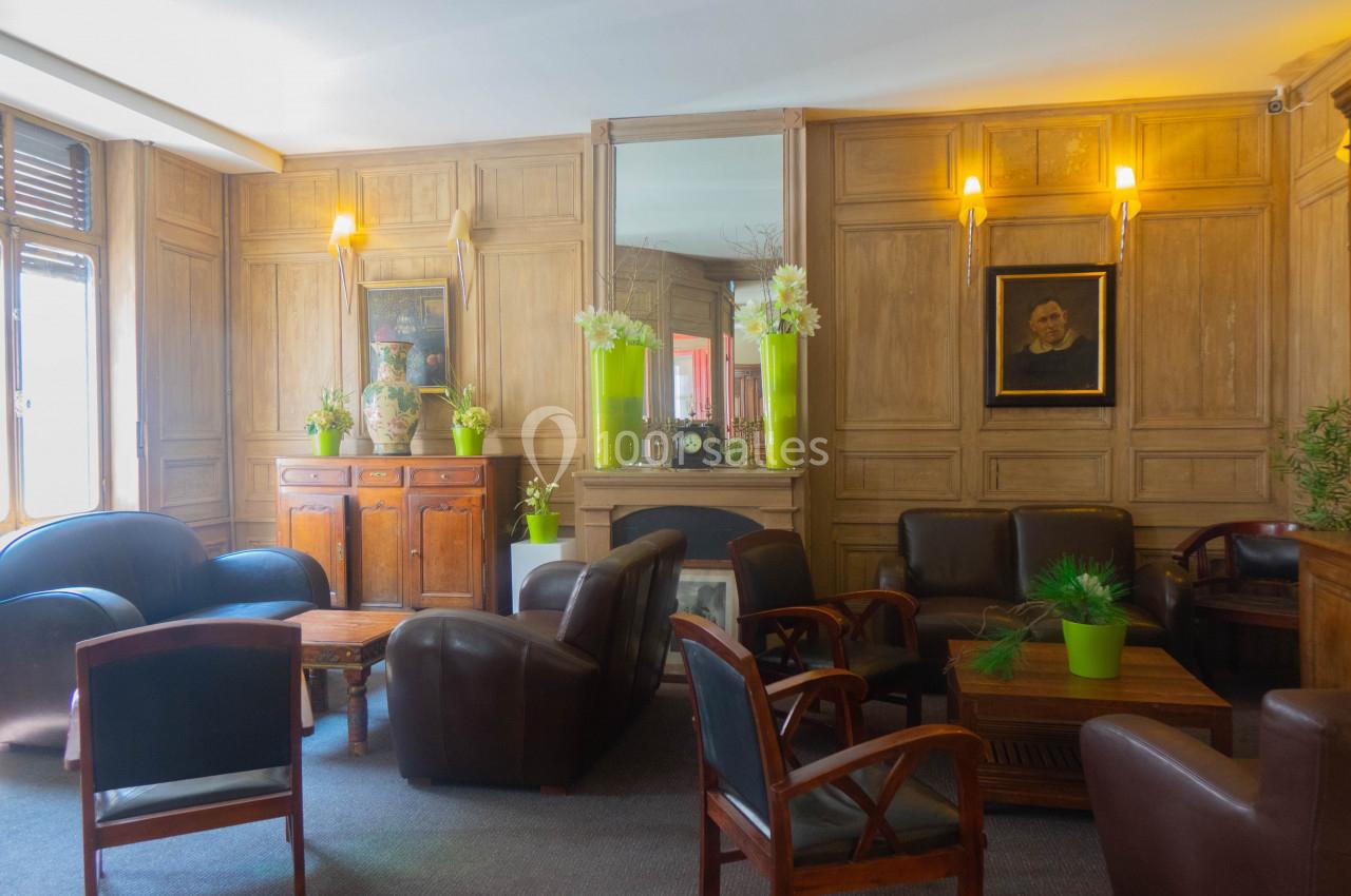 Salon chaleureux avec fauteuils en cuir, cheminée encadrée de miroirs, plantes vertes et boiseries murales.