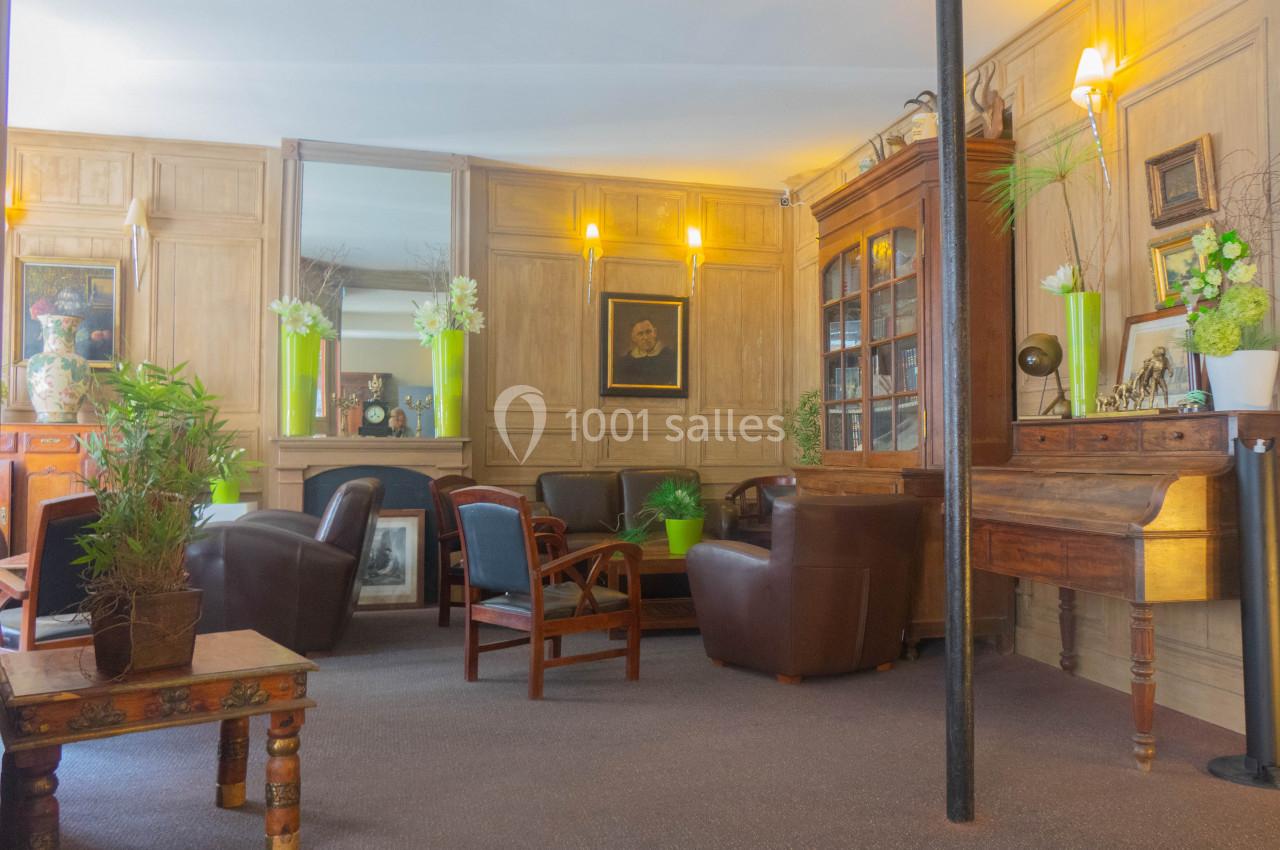 Salon chaleureux avec fauteuils en cuir, table basse en bois, bibliothèque vitrée et décoration végétale.