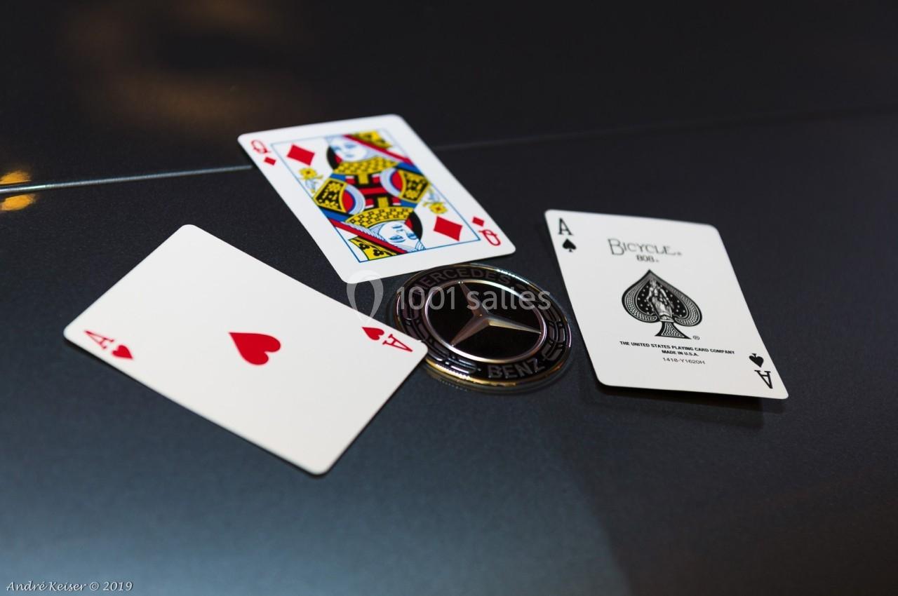 Trois cartes à jouer et un emblème Mercedes-Benz posés sur une surface sombre et réfléchissante.