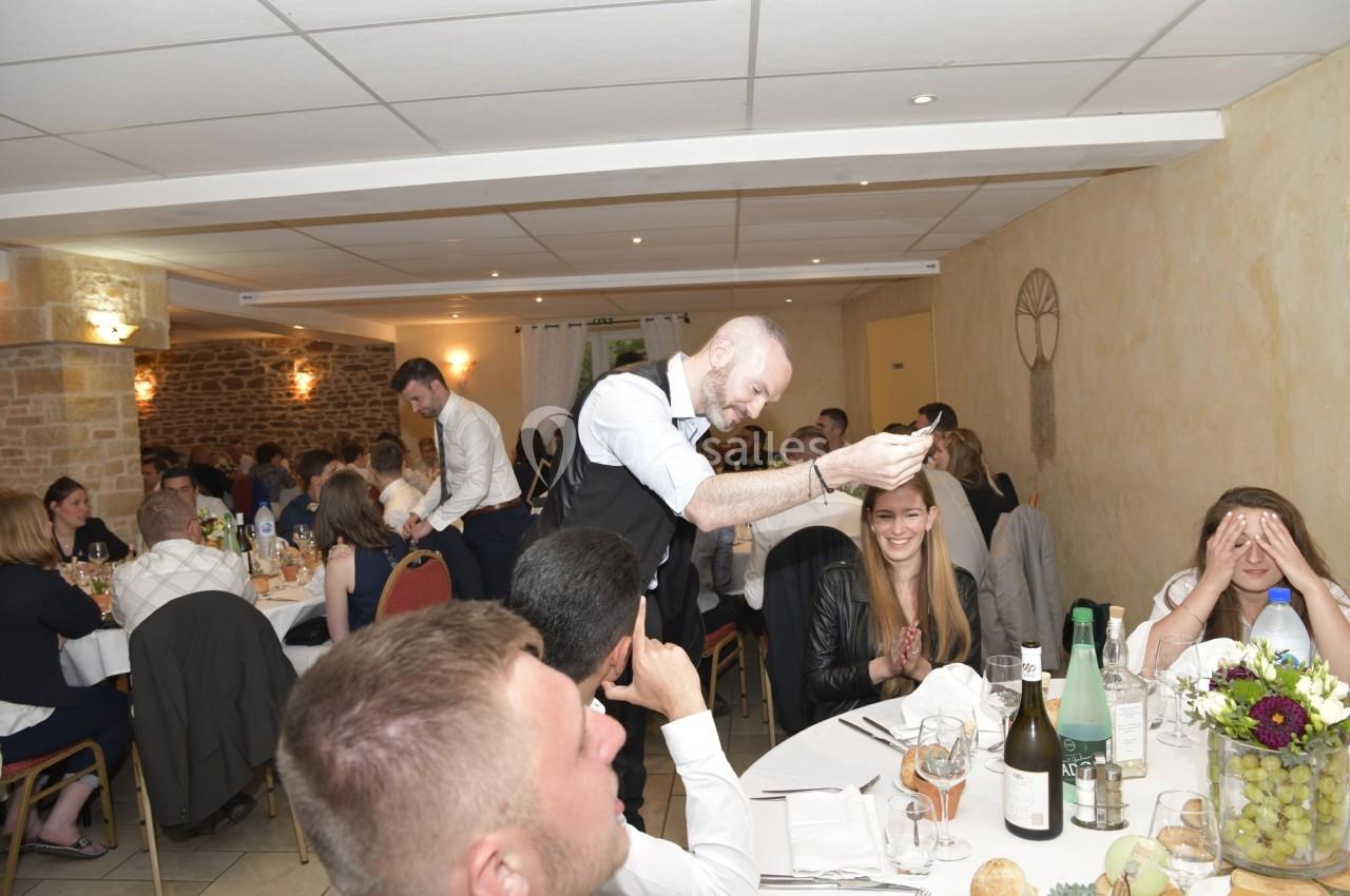 Un homme prend une photo avec un smartphone dans une salle de réception où des invités sont assis à table.