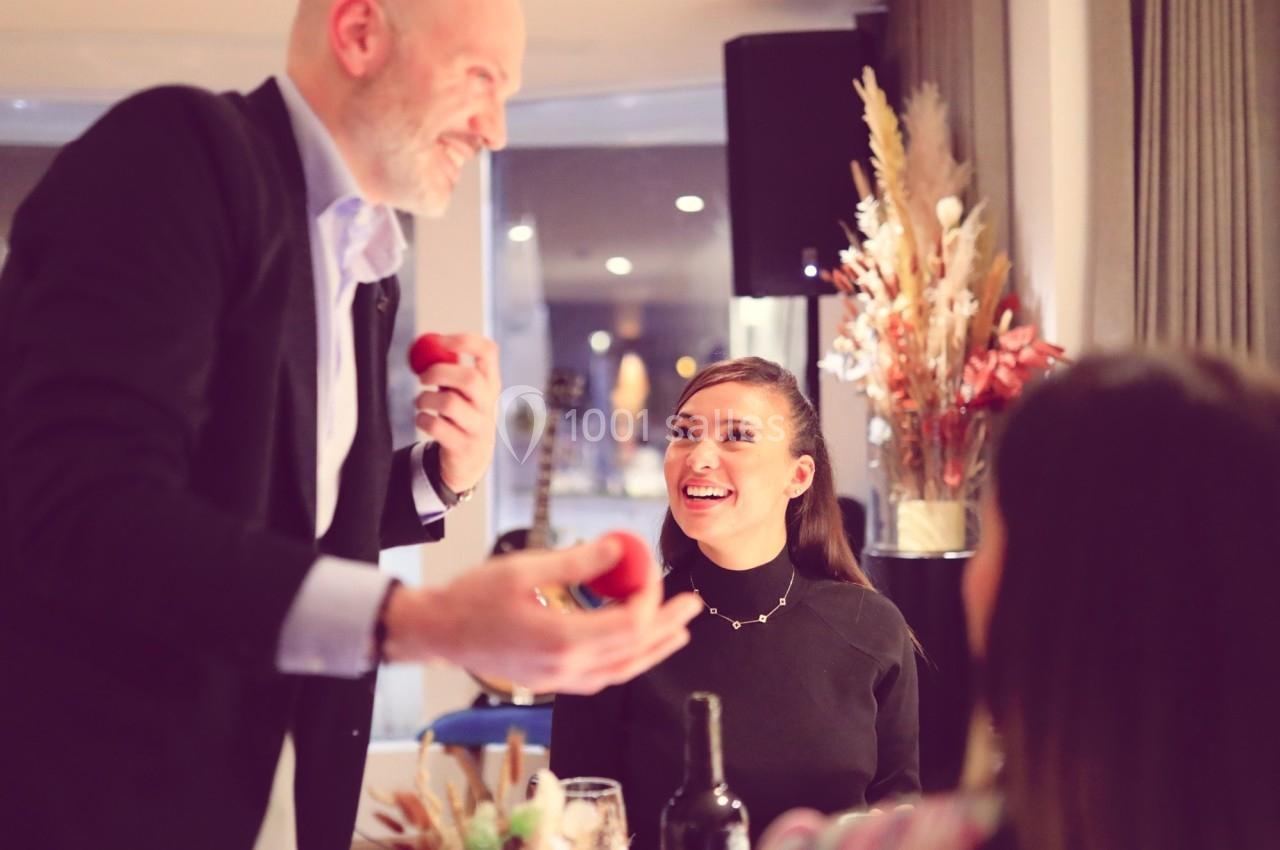Un homme souriant tend un objet rouge à une femme assise à table dans un cadre chaleureux et décoré.