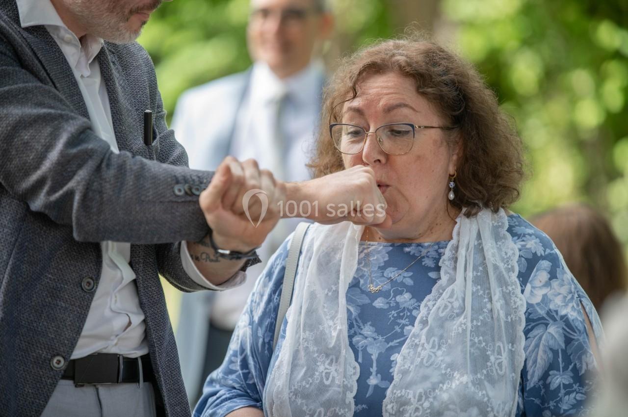 Un homme tend son poignet à une femme qui semble le sentir, dans un environnement extérieur verdoyant.